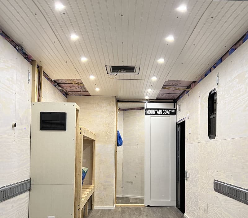 Interior of a camper van with wood paneling, LED lights, and storage areas.