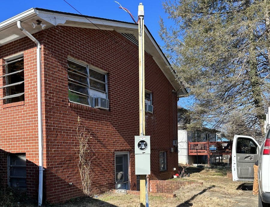 Brick house with utility pole and meter, surrounded by trees on a clear day.