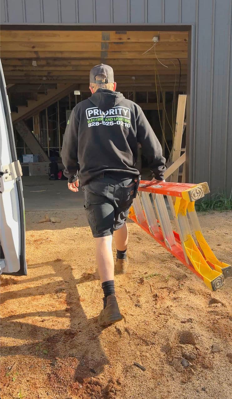 Construction worker carrying a ladder towards a building under renovation.