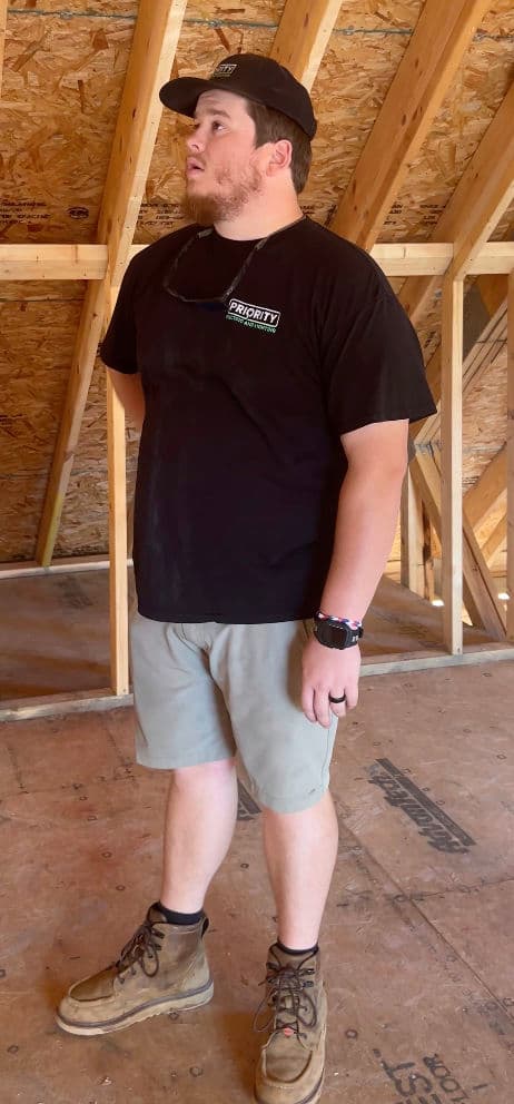 Construction worker in a black shirt and boots standing in a wooden-framed attic.