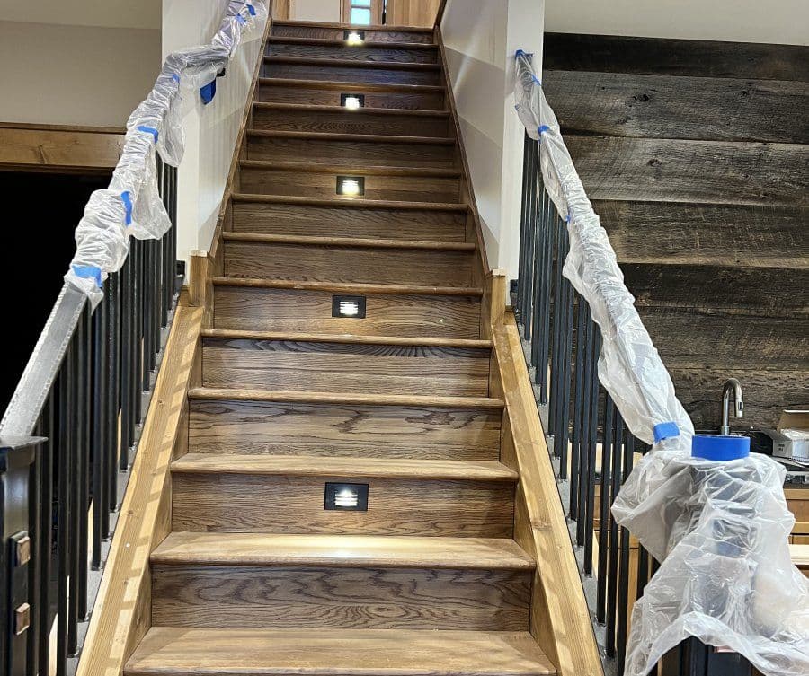 Newly renovated wooden staircase with recessed lighting and protective plastic covering.