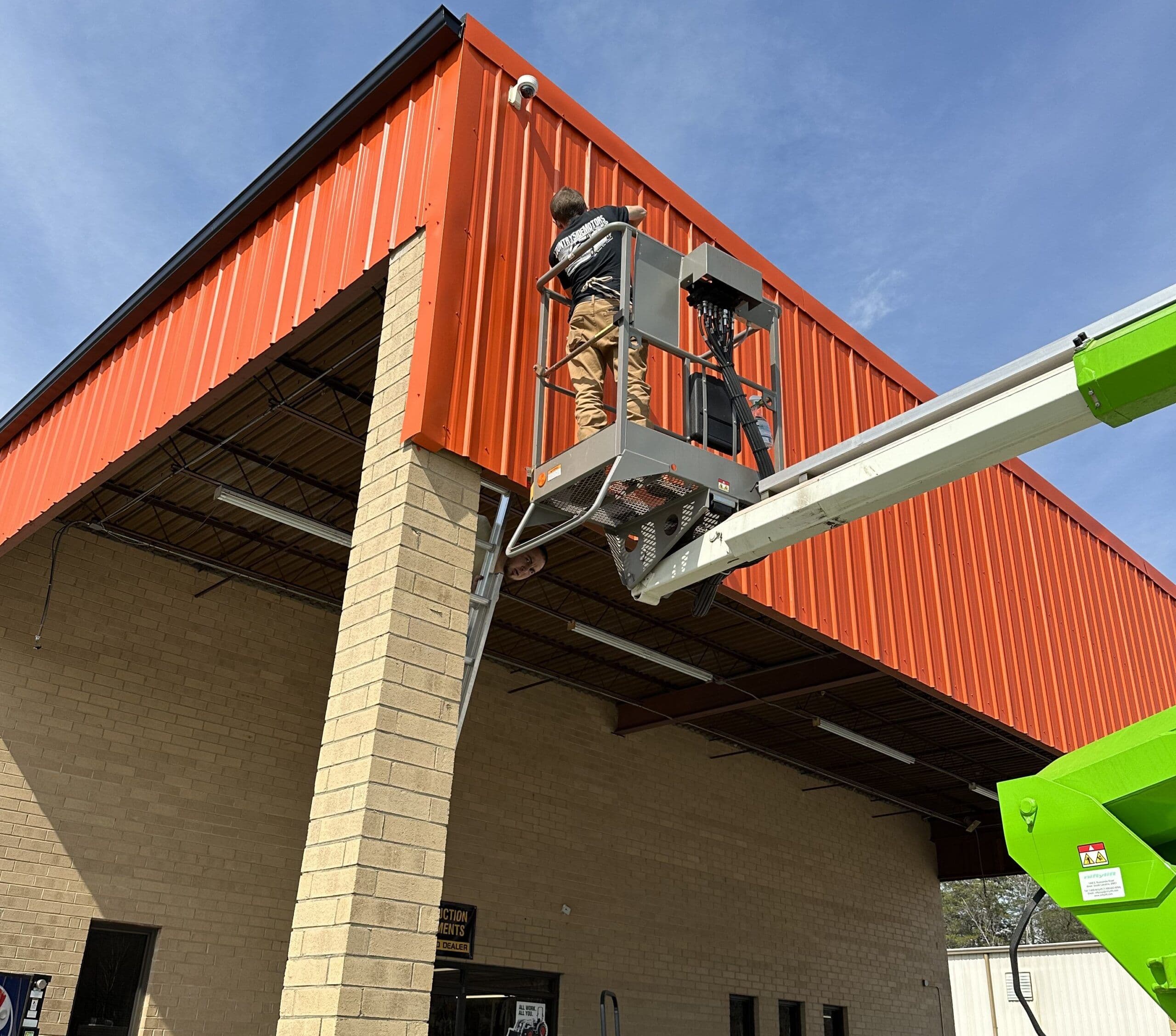 Worker using a lift to install equipment on a bright orange commercial building exterior.