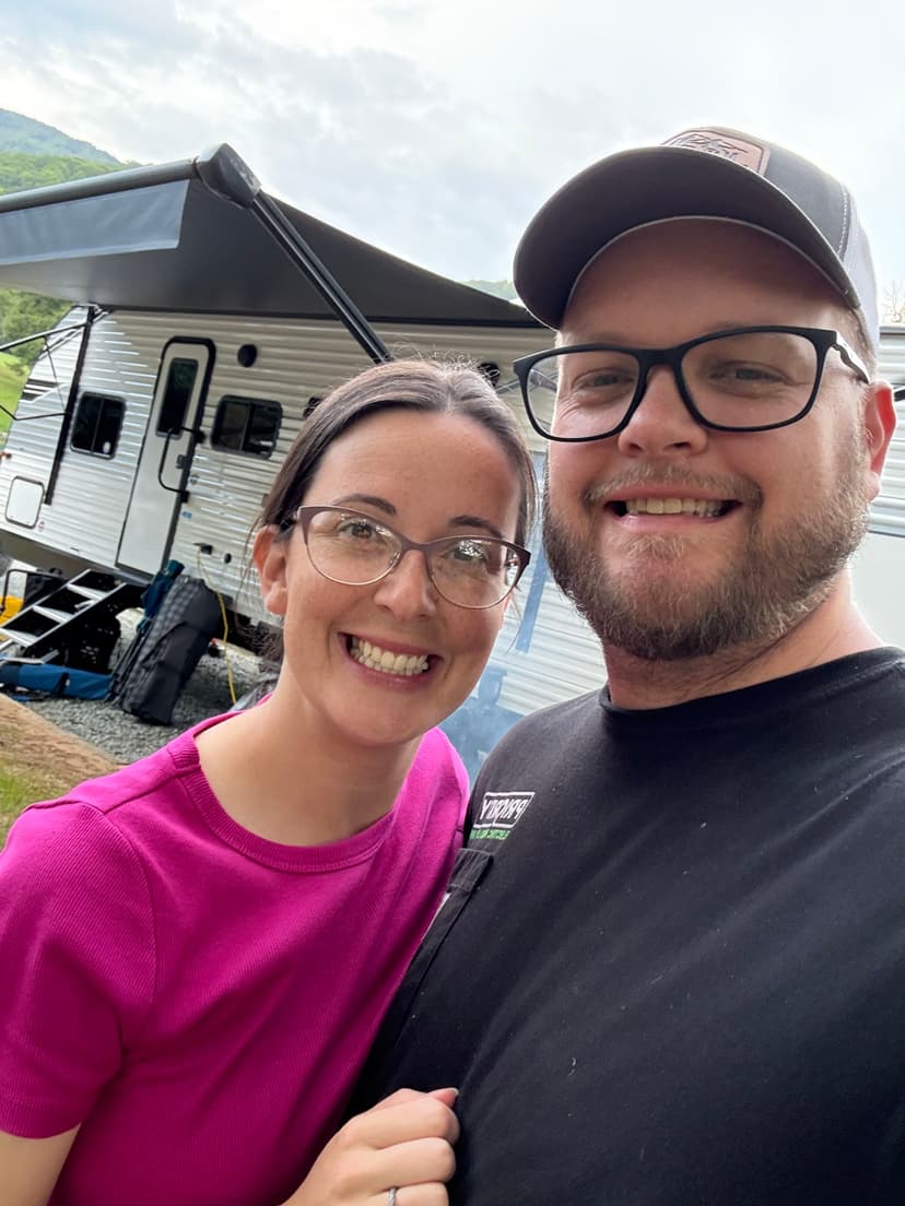 Couple smiling in front of a camper, showcasing outdoor adventure and travel lifestyle.